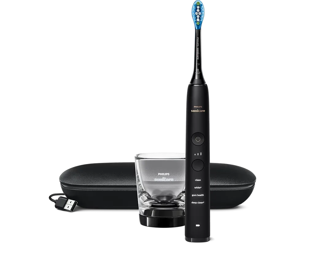 Philips Sonicare DiamondClean 9000 in Schwarz stehend mit aufgestecktem Bürstenkopf und vier beschrifteten Programmen am Griff, davor ein Ladeglas, dahinter ein schwarzes Reiseetui mit USB-Ladekabel